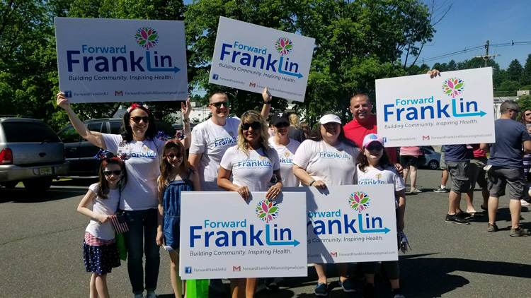 Group of adults and children holding signs for 'Forward Franklin: Building Community. Inspiring Health.' at the Memorial Day parade.