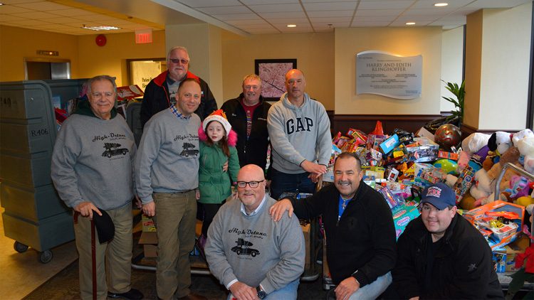 Group of people and child posing next to collected toys for toy drive.