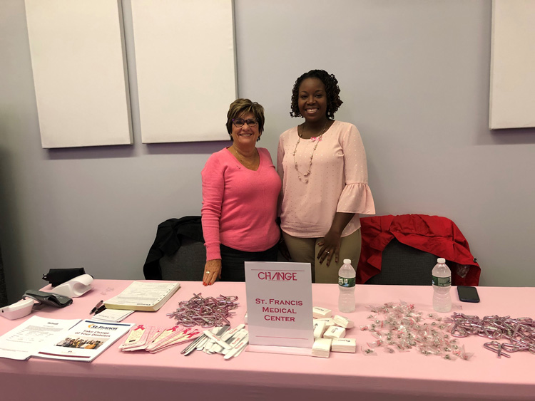 Mary Jo Abbondanza, RN and Sharene Wilson, RN posing behind table with brochures and items for breast cancer awareness.