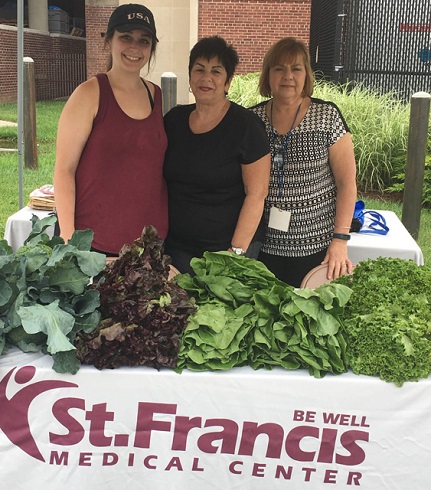 St. Francis Medical Center employees standing behind table with green vegetables for the farmer's market.