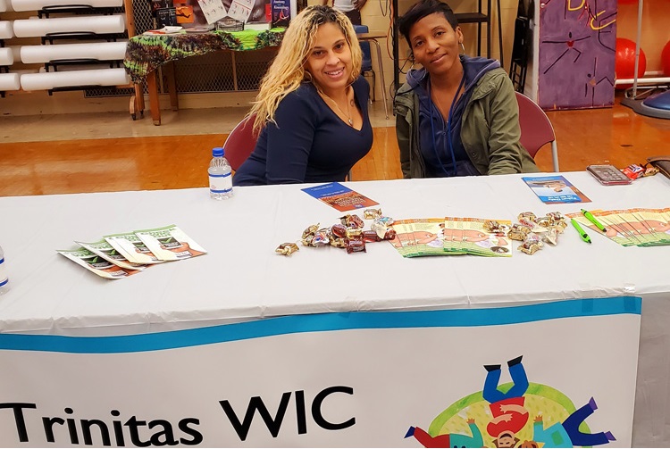 Trinitas employees posing behind information table at the WIC Hillside Health Fair.