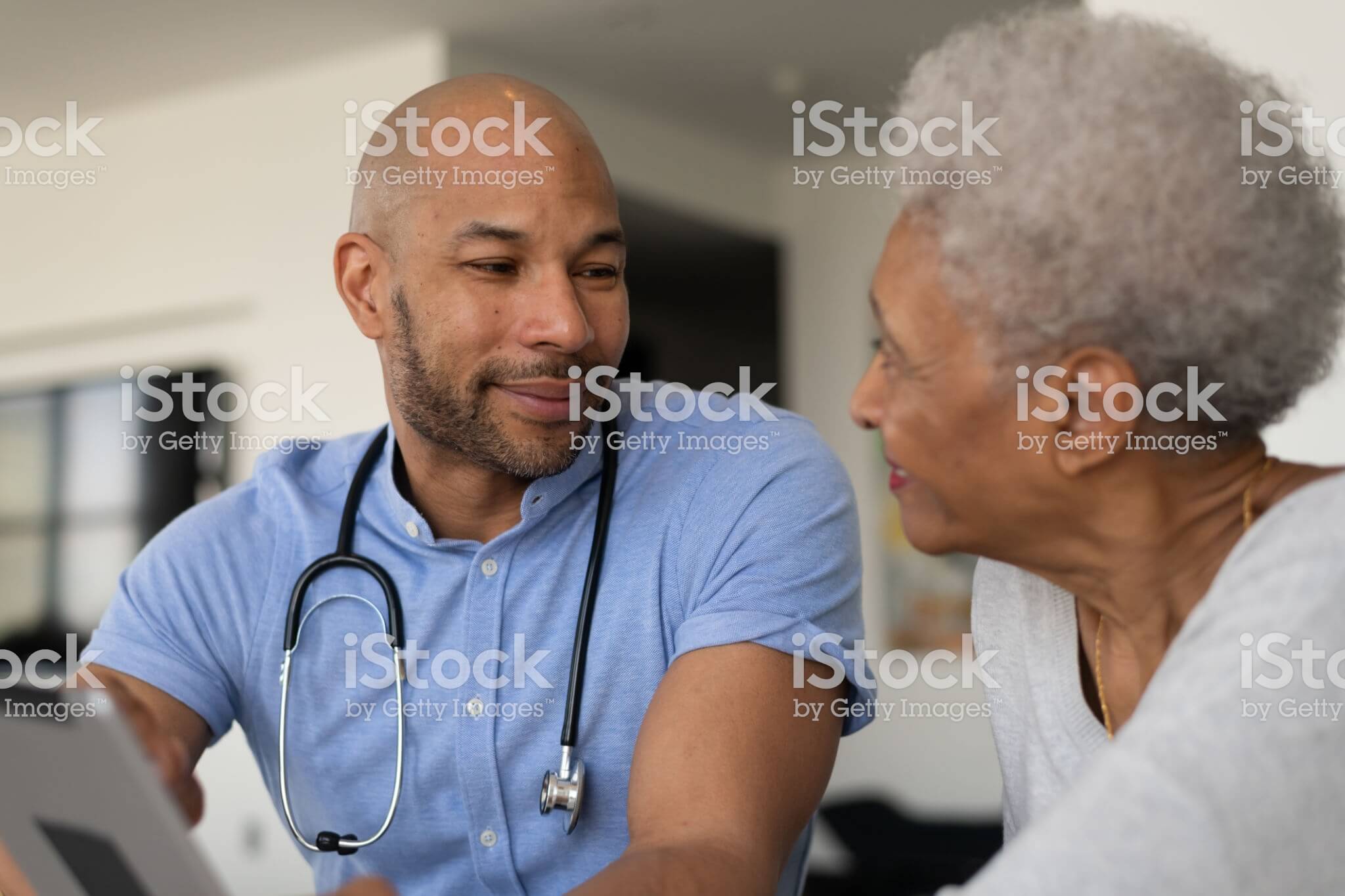 Male doctor speaking with elderly, female patient.