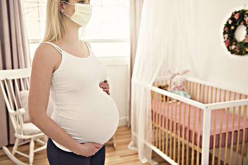 Pregnant person wearing a mask in baby room.