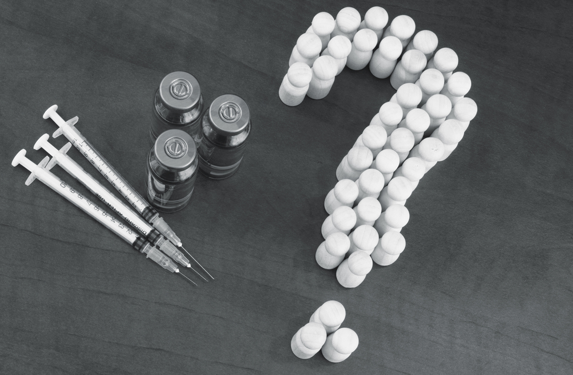 Vaccine vials, syringes and medicine bottles arranged in a question mark.
