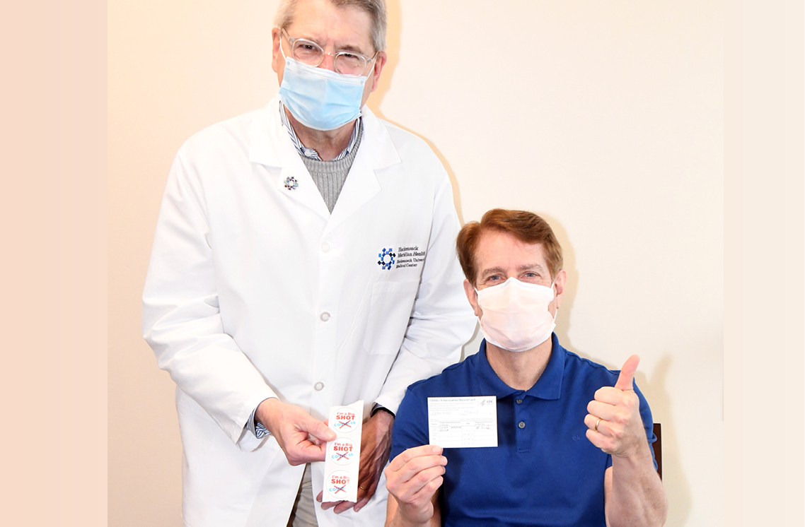 Male healthcare worker holding a roll of I'm a Big Shot stickers and male patient holding sign.