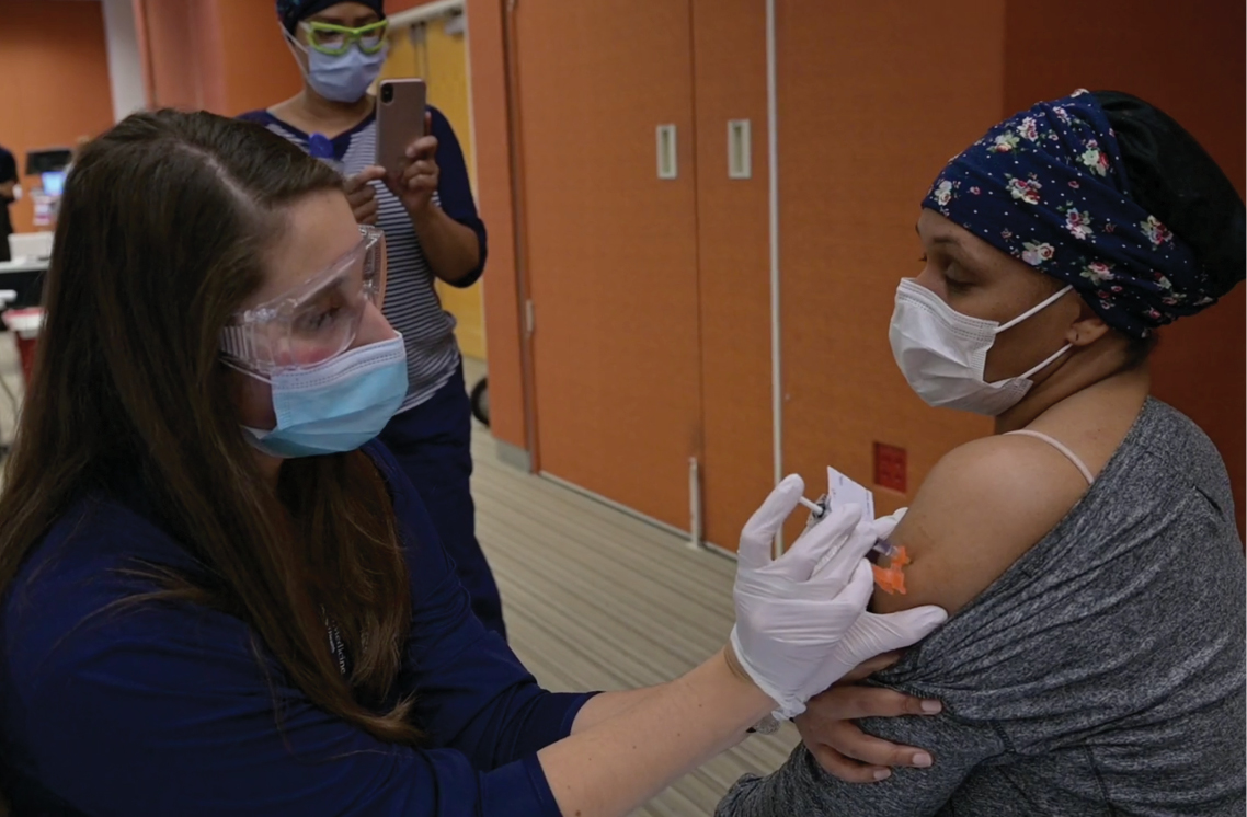 Female healthcare worker administering vaccine to a female patient.