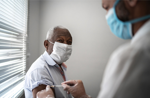 Male senior citizen receiving a shot from medical professional.