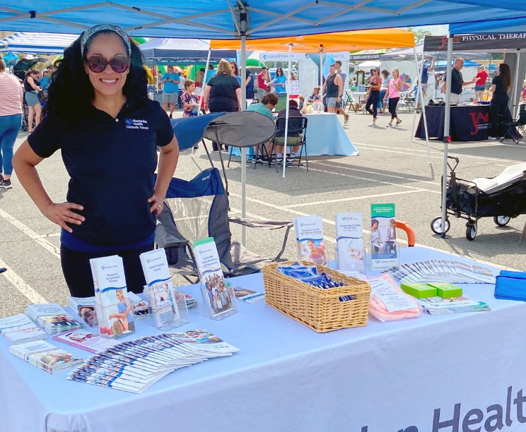 Access to Care featuring an image of a Hunterdon Health staff member standing at a table with informational brochres on it at an outdoor fair